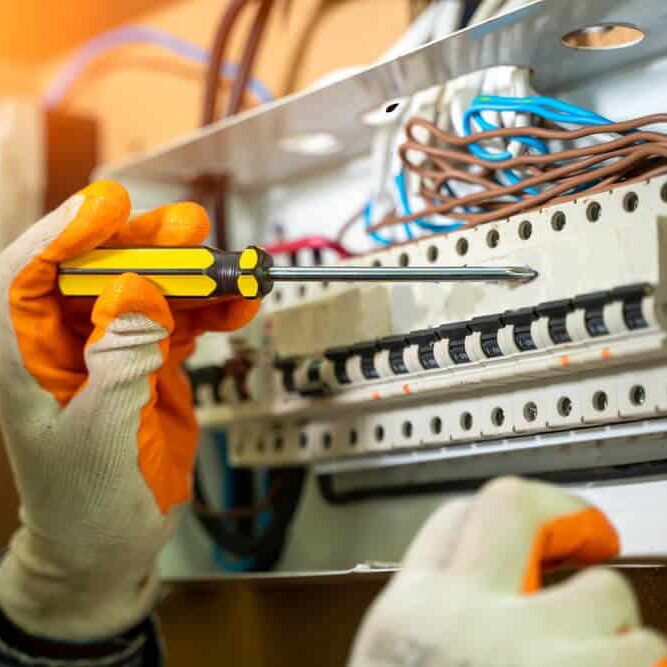 Professional Hot Shot Electric certified electrician repairing breaker box with screwdriver – licensed Tulsa experts fix tripped breakers and upgrade panels for safe, reliable home power in Oklahoma.